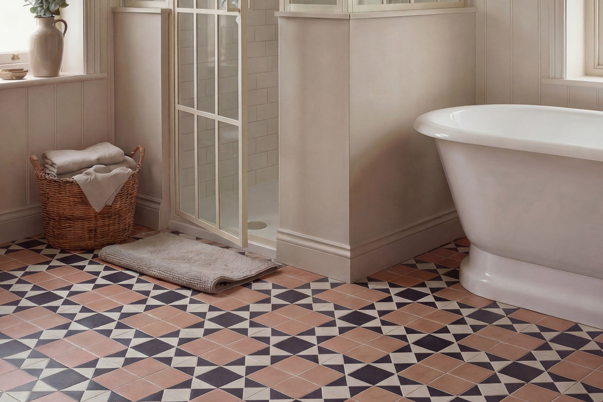 bathroom floor tiled in a terracotta navy and cream geometric pattern with a freestanding roll top bath a woven basket and the base of a glazed shower